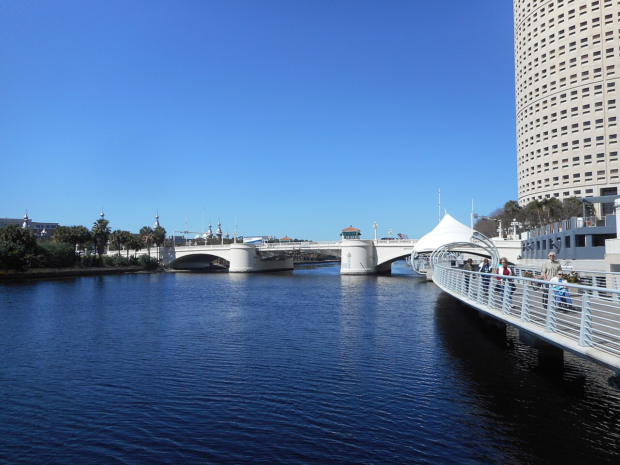 The Tampa Riverwalk curving along the Hillsborough River toward a white bridge